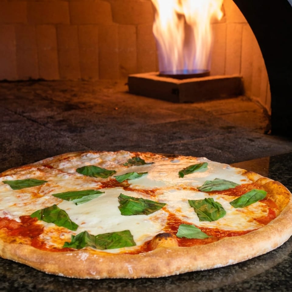 Margherita pizza with melted mozzarella and fresh basil rests before a glowing wood-fired oven.